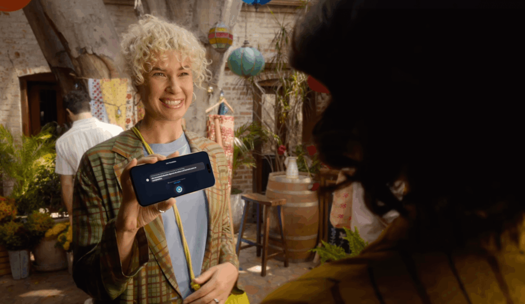 Smiling woman showing iPhone 17 with real-time translation feature activated, standing in a colorful outdoor courtyard.