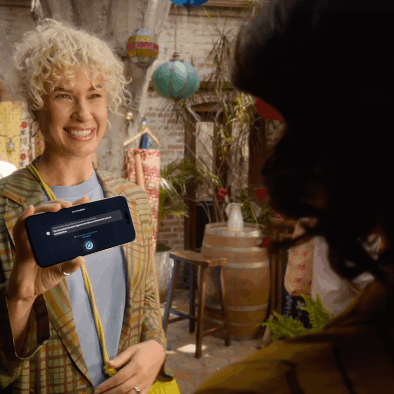 Smiling woman showing iPhone 17 with real-time translation feature activated, standing in a colorful outdoor courtyard.