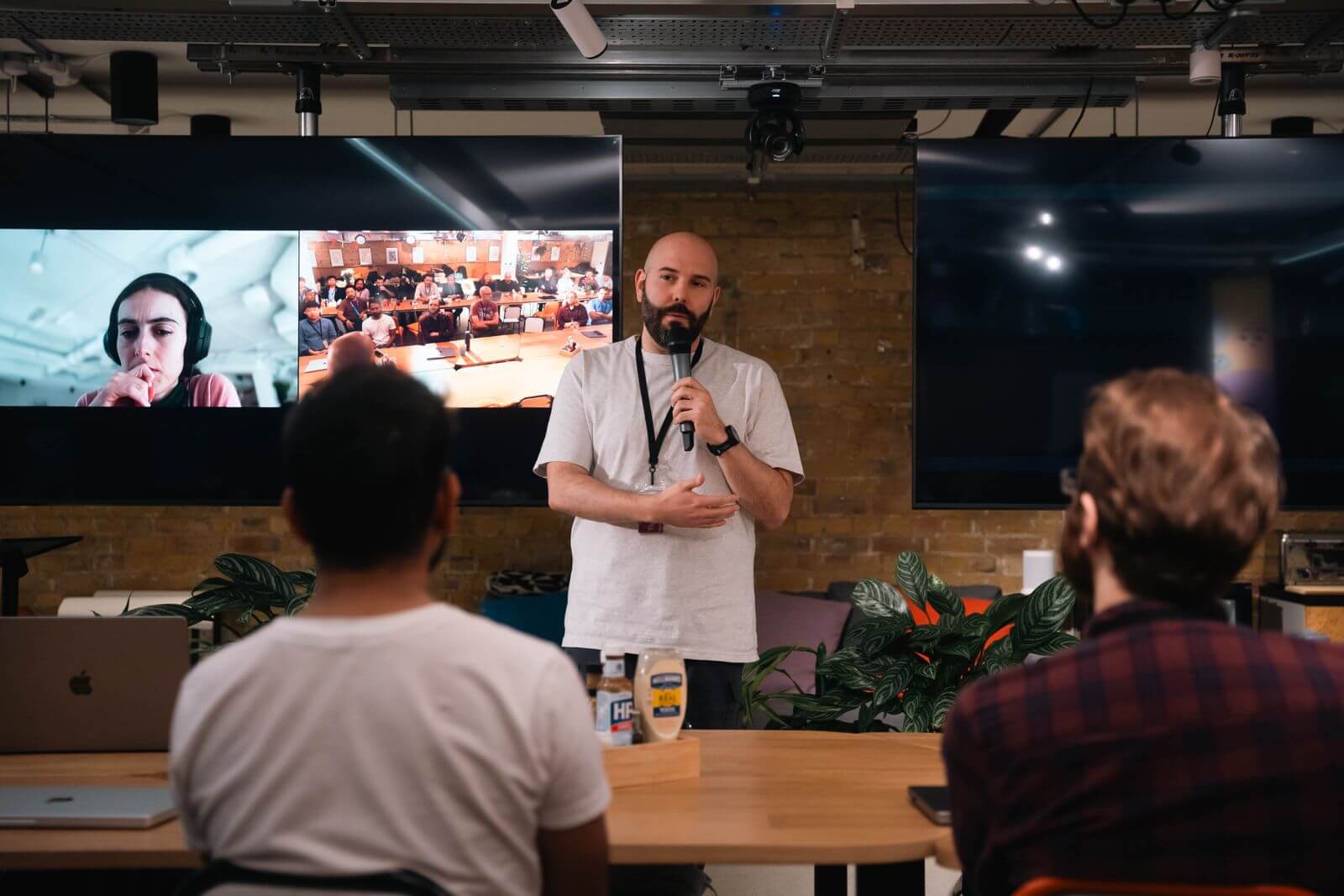 A presenter addressing in-room participants and remote attendees shown on a screen.